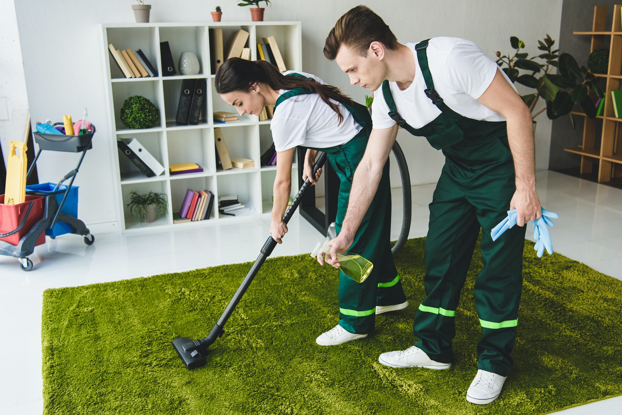 young cleaning company workers cleaning carpet with vacuum cleaner and detergent spray